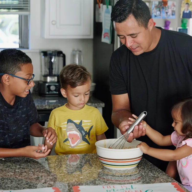 Kids in kitchen gathered around mixing bowl