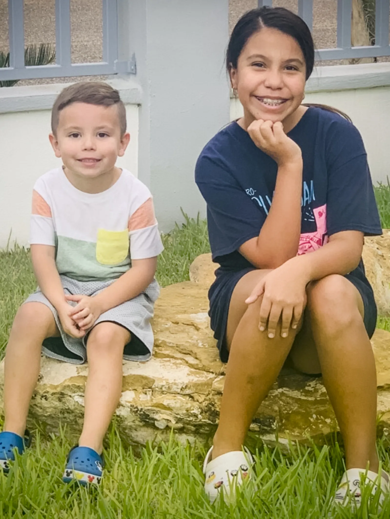 René and Julien De Luna smile, sitting atop a rock in grass.