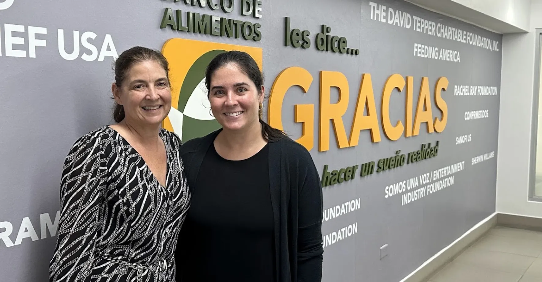 Two women in front of mural that says Gracias