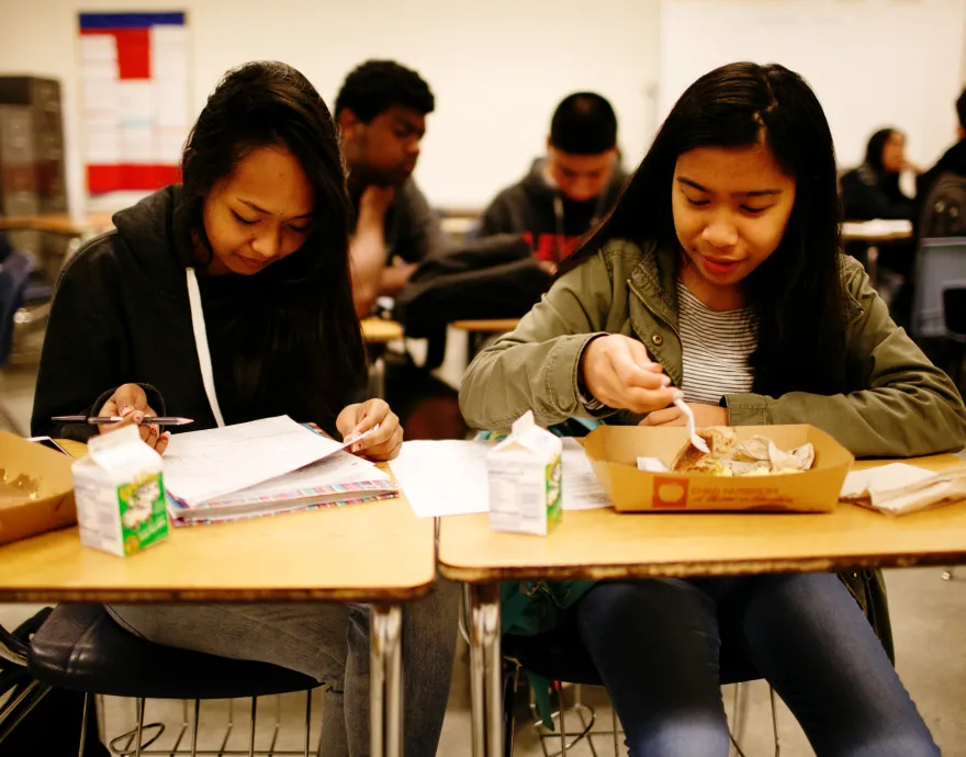 Two girls eating breakfast at their desks