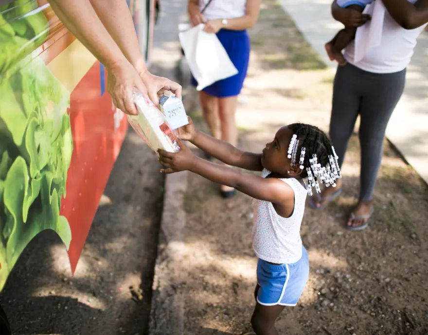 A little girl getting a free summer meal from a mobile meals truck