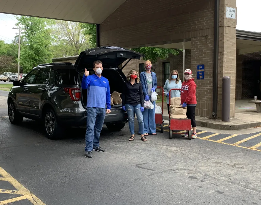 People in face masks stand behind an SUV that they're loading with sacks of food.