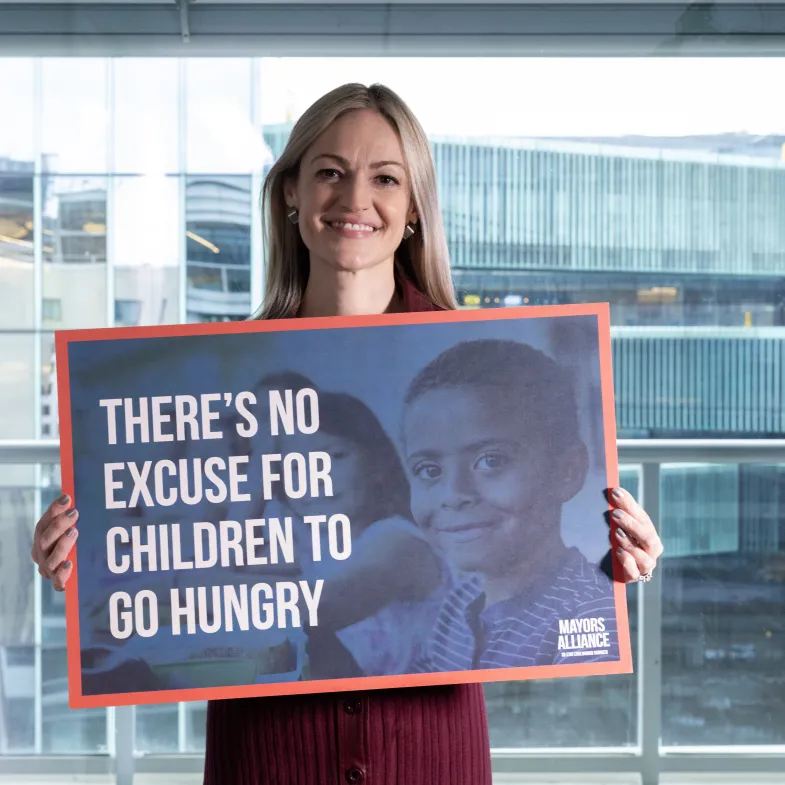 Mayor Cognetti (white woman) Holding sign saying there is no excuse for children to go hungry