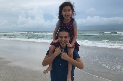 Man on beach with daughter on shoulders