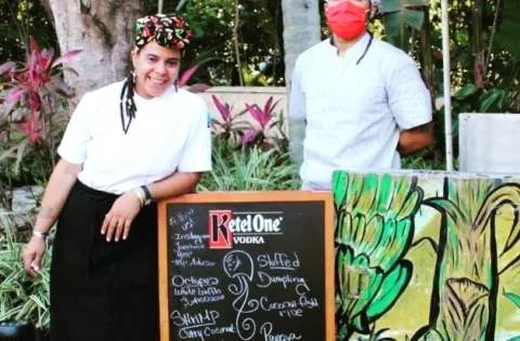 Two people wearing masks in front of food sign