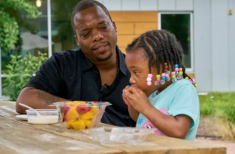 Father looking at her daughter eating a bowl of fruit