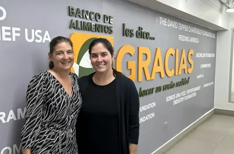 Two women in front of mural that says Gracias